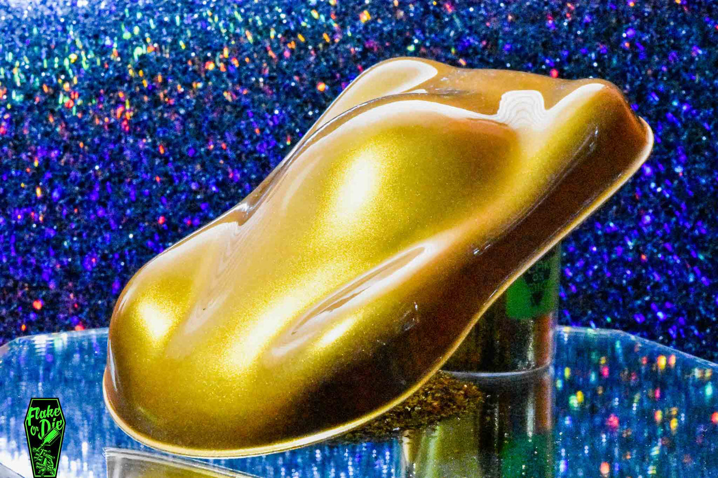 Macro photography of a car like speed shape painted with gold pearl pigment. Lighting contrast on the curves of the shape. Mirrored platform and complementary background of blue bokeh.