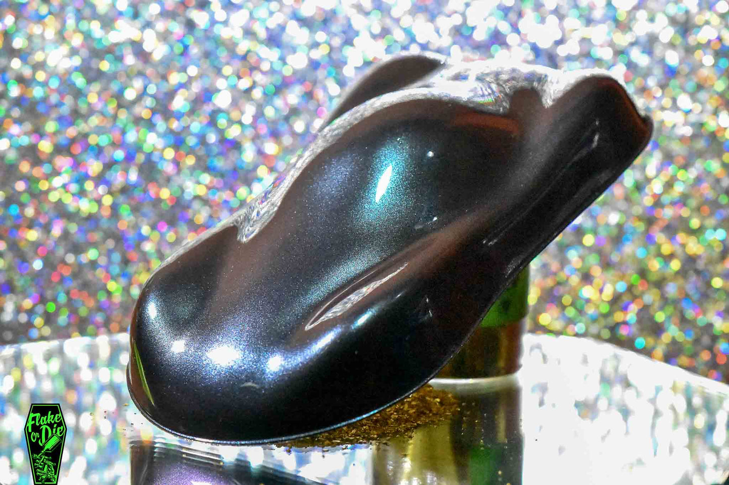 Macro photography of a car like speed shape painted with black colorshift pearl pigment. Lighting contrasts of black, teal, and blue on the curves of the shape. Mirrored platform and complementary background of silver bokeh.