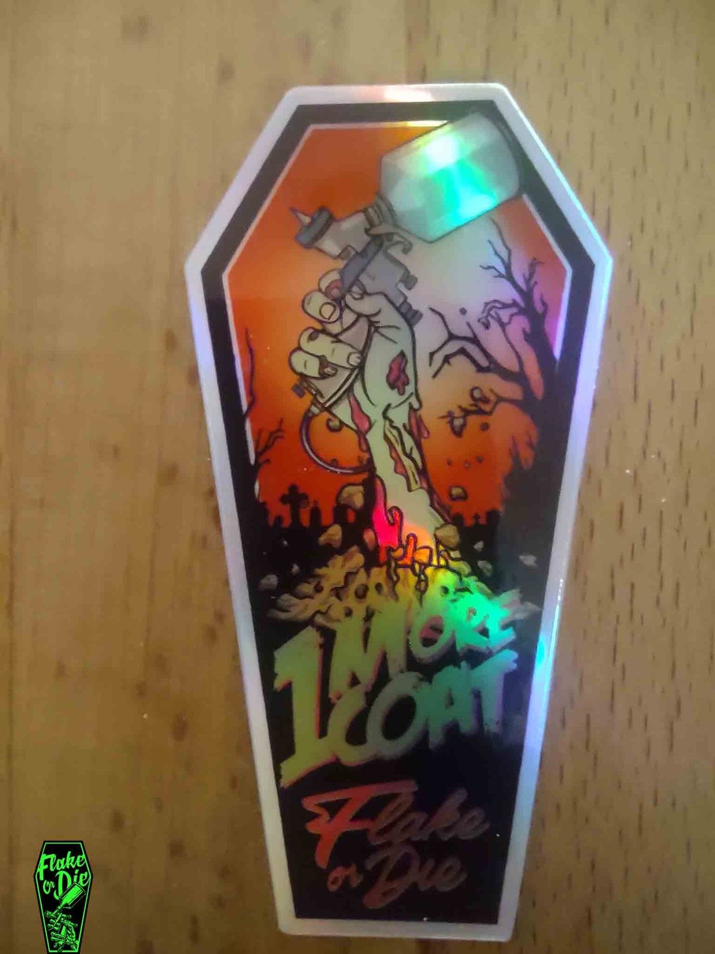 3"x1.5" holographic coffin sticker featuring our new zombie design. Zombie hand with a paint sprayer in a graveyard background.