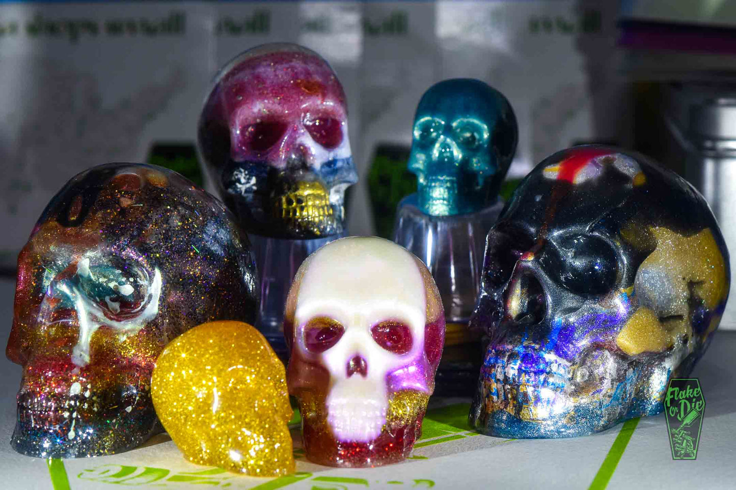 Various sized skulls cast with metal flake, pearl pigments and crushed glass in clear liquid plastic.