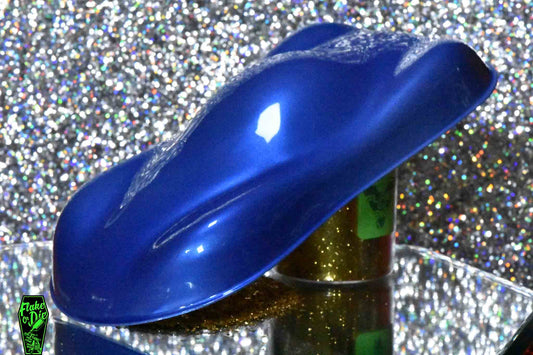 Macro photography of a car like speed shape painted with blue pearl pigment. Lighting contrasts on the curves of the shape. Mirrored platform and complementary background of silver bokeh.