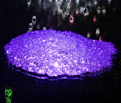 Macro photography of a small pile of blended purple metal flake particles. Distinct glitter flares on the metal flake and a complementary background of silver/black bokeh.