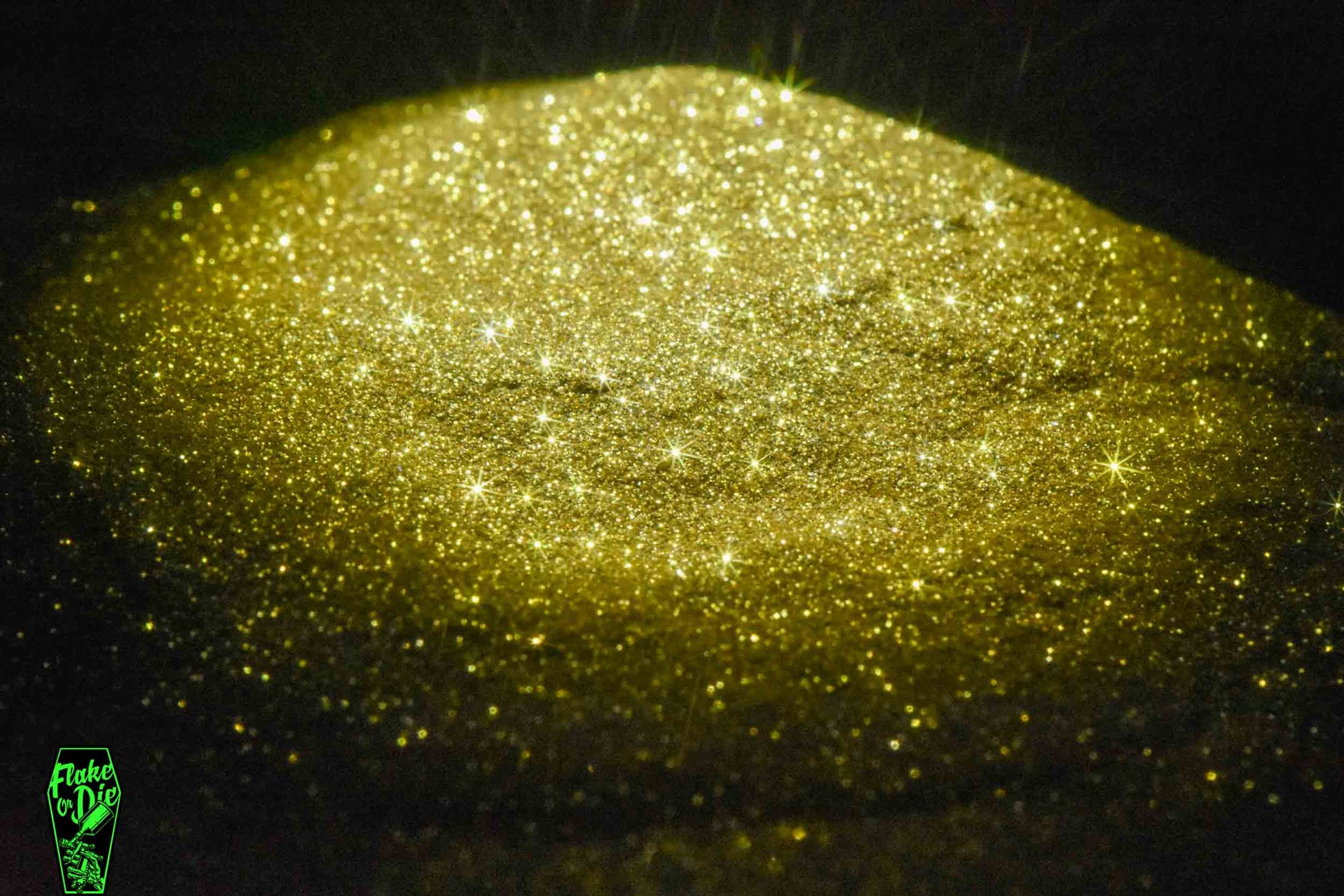 Macro photography of a small pile of gold metal flake particles. Distinct glitter flares on the metal flake and a dark background.
