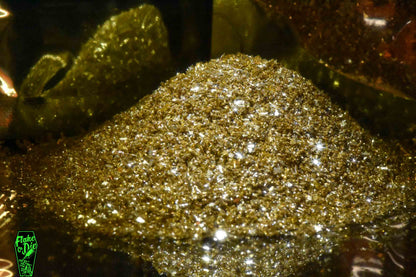 Macro photography of a small pile of gold mirrored glass particles. Distinct glitter flares of gold shards.