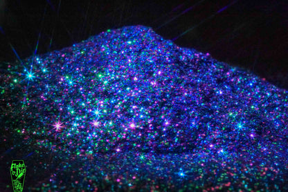 Macro photography of a small pile of blended magenta, green, blue metal flake particles. Distinct glitter flares on the metal flake and a complementary black background.