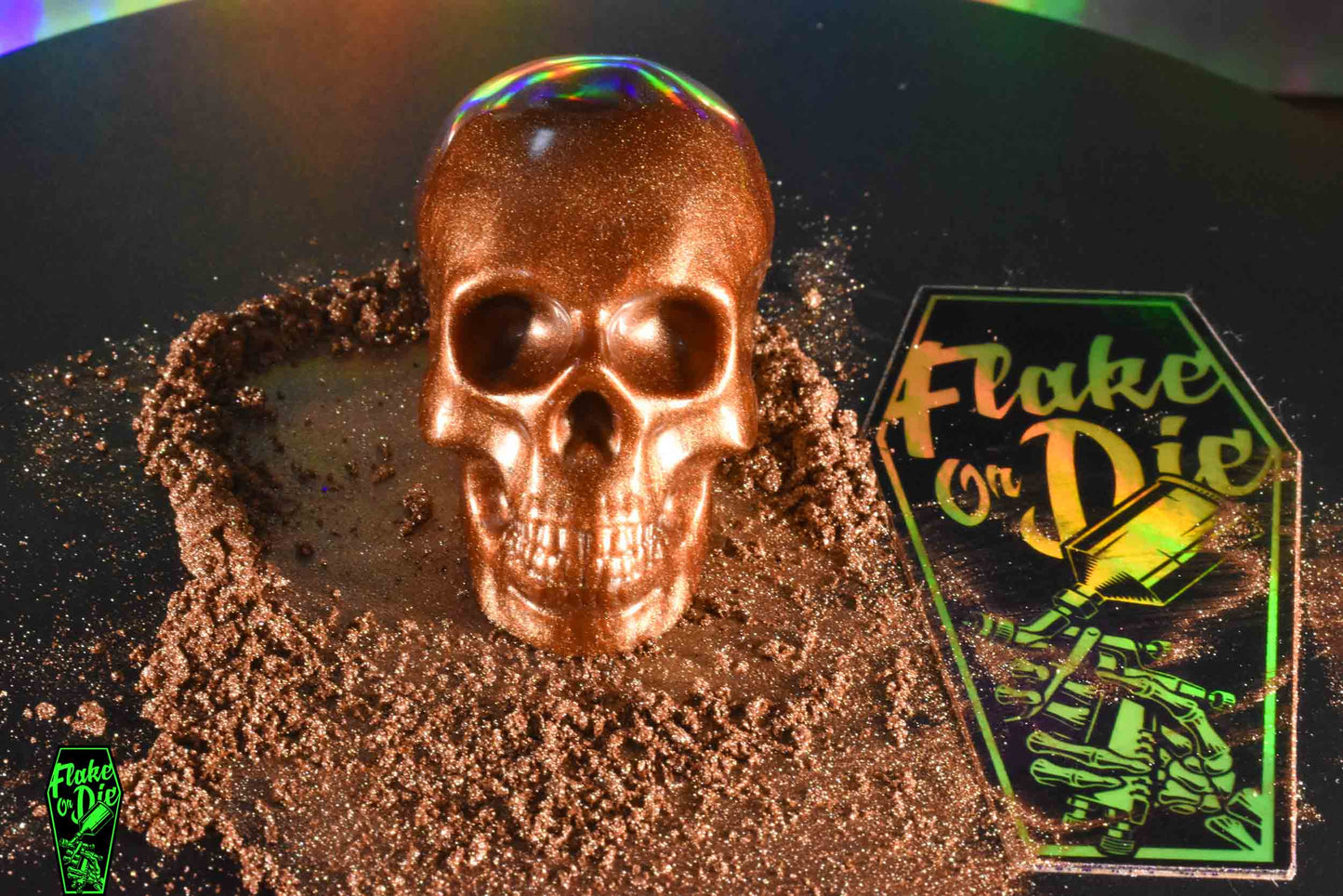 Brown pearl pigment spread over black background, with Flake or Die sticker and a resin skull made with Skunk Ape brown pearl pigment.