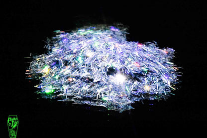 Macro photography of a small pile of silver holographic splinter cut metal flake particles. Distinct glitter flares of yellow, green, red and orange on the metal flake and a stark black background.