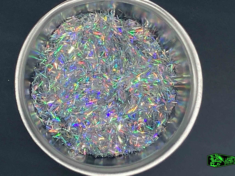 Direct macro photography shot of silver holographic splinter cut metal flake particles with rainbow shimmers in a stainless-steel bowl.