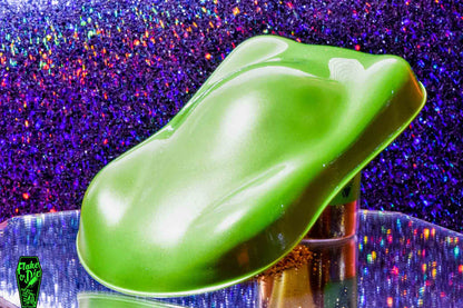 Macro photography of a car like speed shape painted with lime green pearl pigment. The lighting contrasts dark and light lime green on the curves of the shape. Mirrored platform and complementary background of blue/rainebow bokeh.