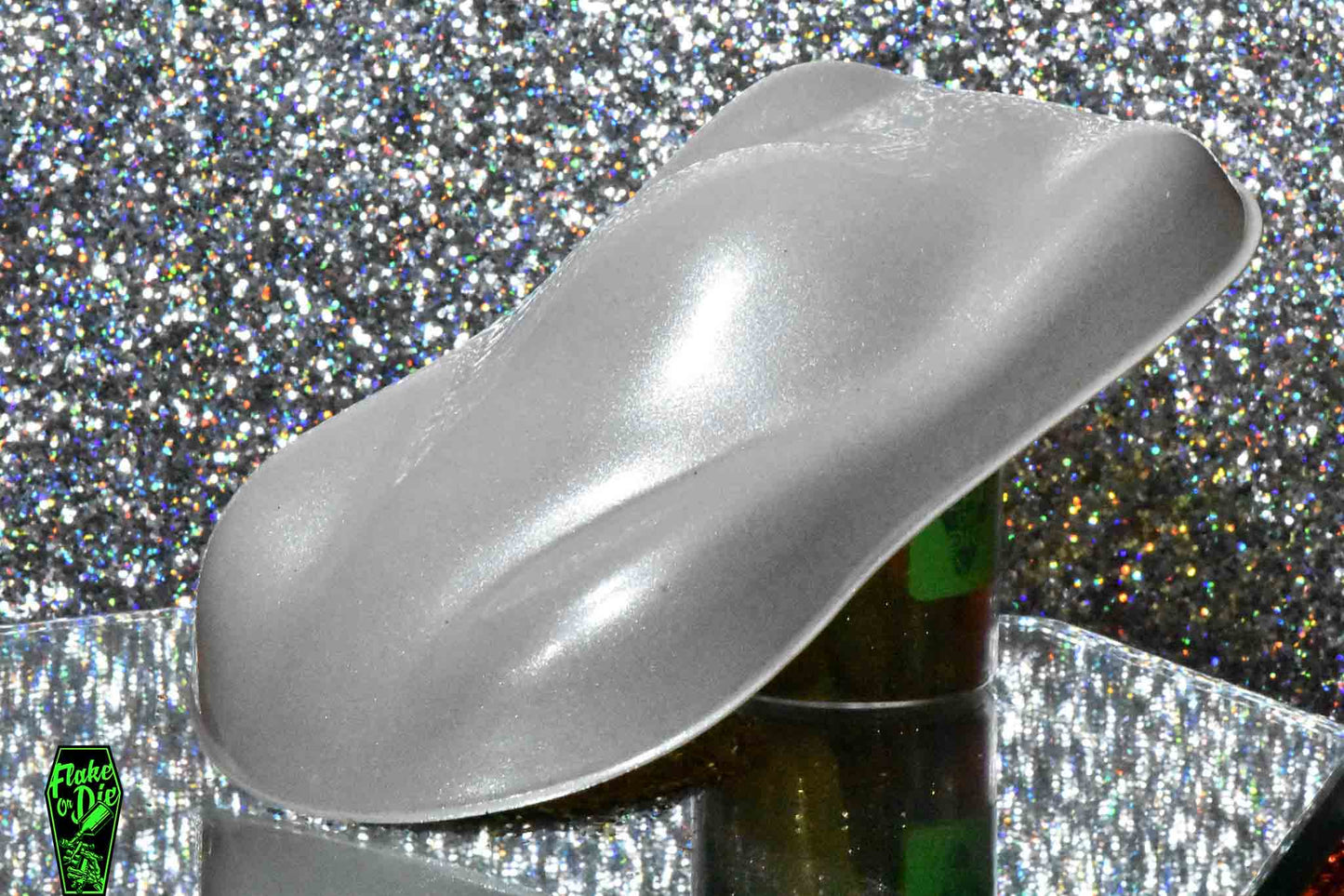 Macro photography of a car like speed shape painted with silver pearl pigment. The lighting contrasts dark and light silver on the curves of the shape. Mirrored platform and complementary background of silver bokeh.